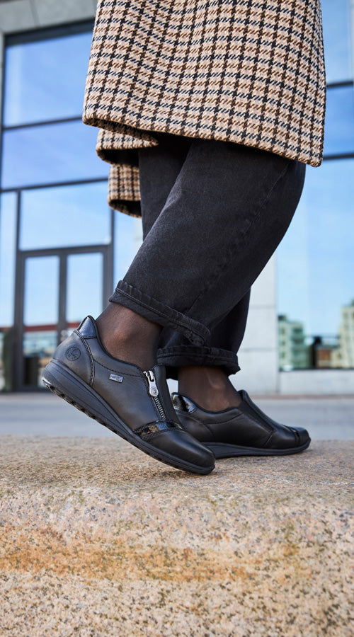 Person wearing black shoes and a checkered coat on a city street.