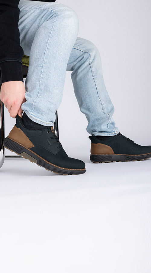 Person wearing black and brown shoes with light blue jeans on a white background